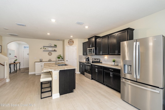 kitchen with sink, a breakfast bar area, appliances with stainless steel finishes, light stone countertops, and a center island with sink