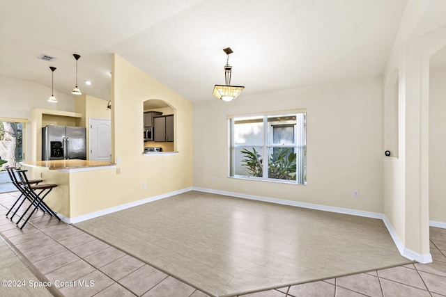 interior space featuring a breakfast bar area, pendant lighting, vaulted ceiling, and appliances with stainless steel finishes