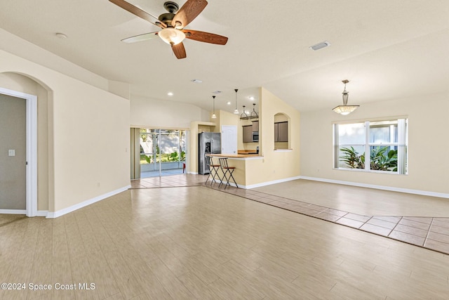 unfurnished living room with ceiling fan, vaulted ceiling, and light wood-type flooring