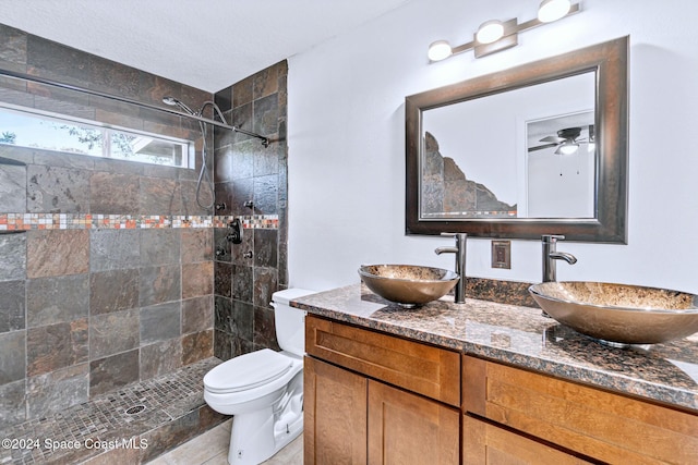 bathroom with tiled shower, vanity, toilet, and ceiling fan