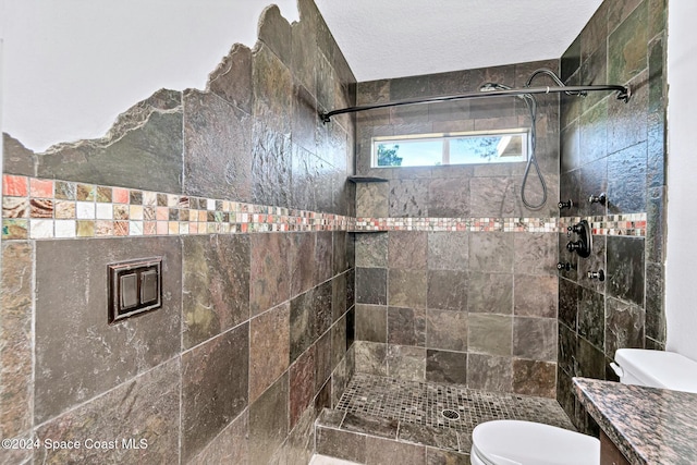 bathroom with a tile shower, vanity, and toilet