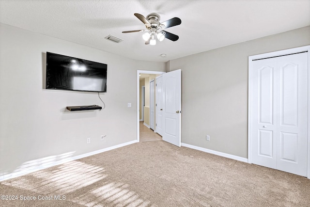 unfurnished bedroom featuring ceiling fan, light colored carpet, a textured ceiling, and a closet