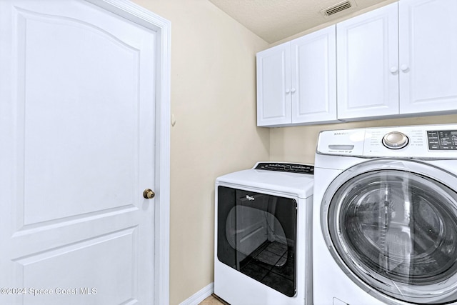 laundry room featuring washer and clothes dryer, cabinets, and a textured ceiling