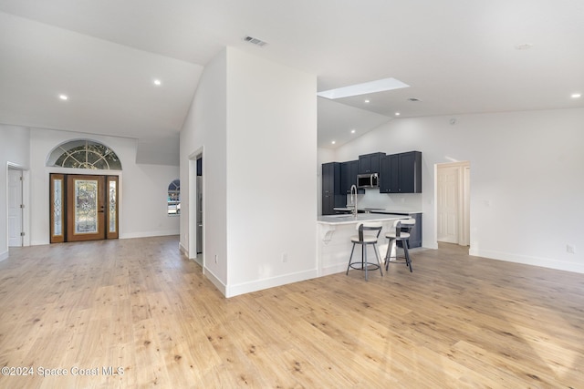 kitchen with sink, high vaulted ceiling, light hardwood / wood-style floors, a breakfast bar area, and an island with sink