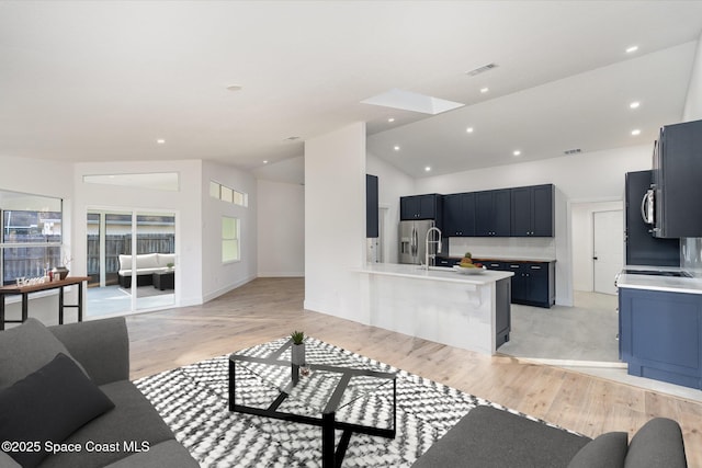 living room featuring light wood-type flooring, sink, and high vaulted ceiling