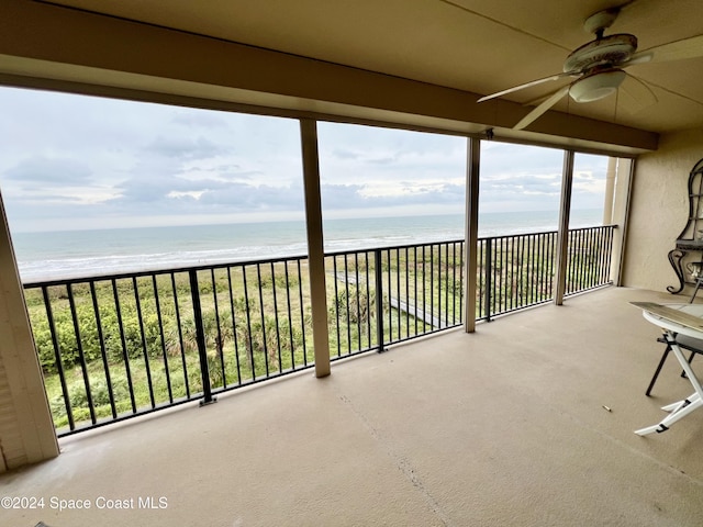 unfurnished sunroom with ceiling fan, a water view, and a view of the beach