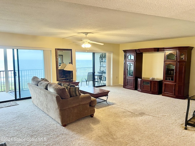 living room with carpet, ceiling fan, a water view, and a textured ceiling