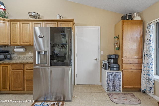 kitchen with a textured ceiling, stainless steel fridge with ice dispenser, light tile patterned floors, and lofted ceiling