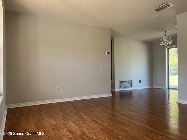 spare room with dark hardwood / wood-style floors and a chandelier