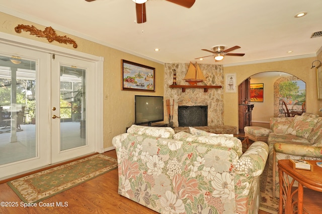 living room featuring ceiling fan, wood-type flooring, crown molding, and a stone fireplace