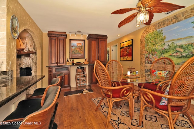 dining room with ceiling fan, track lighting, a fireplace, and hardwood / wood-style floors