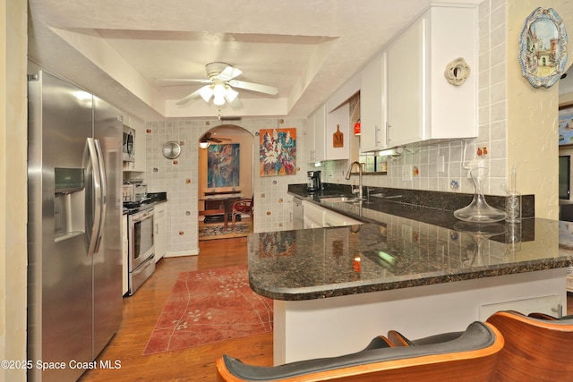 kitchen with kitchen peninsula, appliances with stainless steel finishes, a tray ceiling, and white cabinetry