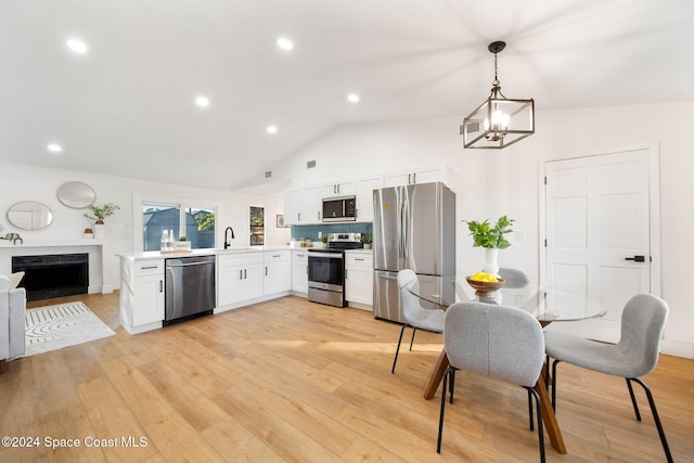 kitchen featuring white cabinets, stainless steel appliances, decorative light fixtures, and light hardwood / wood-style floors