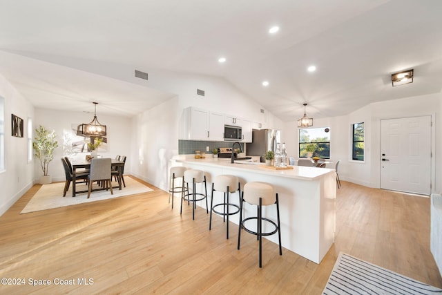 kitchen with pendant lighting, a breakfast bar area, light hardwood / wood-style floors, white cabinetry, and lofted ceiling