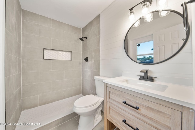 bathroom with vanity, tile patterned floors, toilet, tiled shower, and tile walls