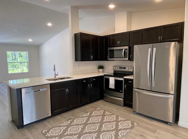 kitchen with kitchen peninsula, lofted ceiling, stainless steel appliances, and light hardwood / wood-style flooring