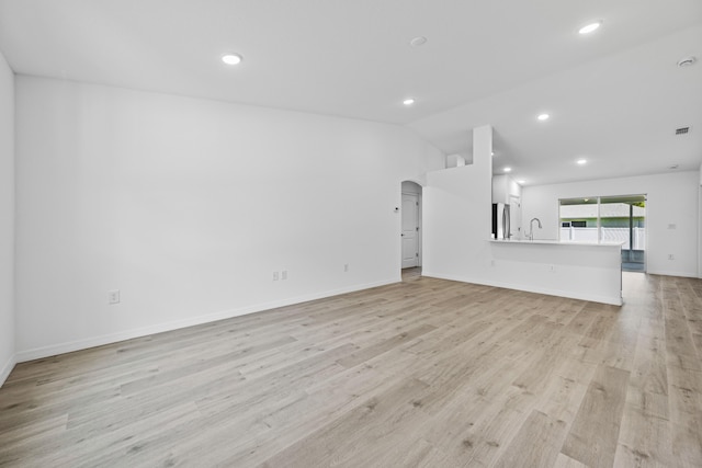 unfurnished living room featuring light wood-type flooring, lofted ceiling, and sink