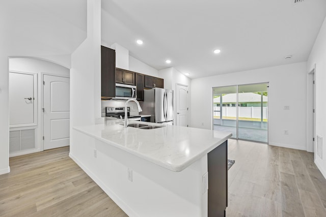 kitchen with a kitchen bar, appliances with stainless steel finishes, dark brown cabinets, light hardwood / wood-style floors, and lofted ceiling