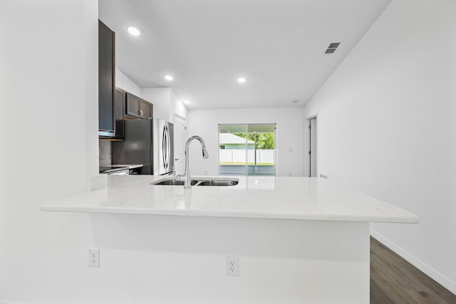 kitchen featuring kitchen peninsula, light stone counters, sink, and dark wood-type flooring