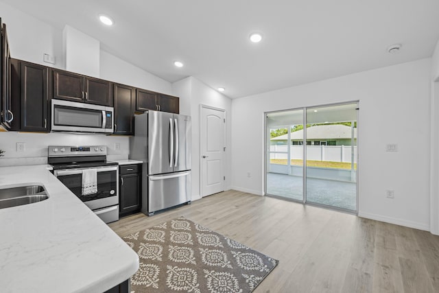 kitchen with appliances with stainless steel finishes, light stone counters, dark brown cabinetry, light hardwood / wood-style flooring, and lofted ceiling