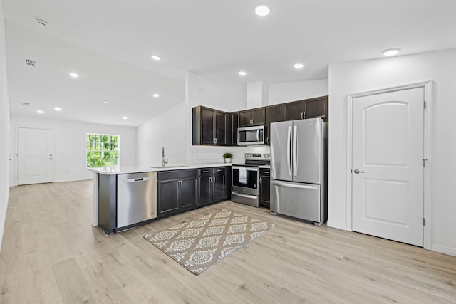 kitchen featuring kitchen peninsula, stainless steel appliances, vaulted ceiling, sink, and light hardwood / wood-style floors