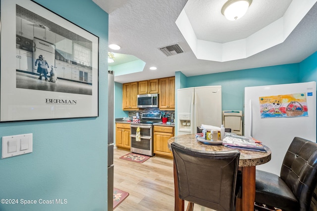 kitchen featuring tasteful backsplash, a textured ceiling, a tray ceiling, light hardwood / wood-style floors, and stainless steel appliances