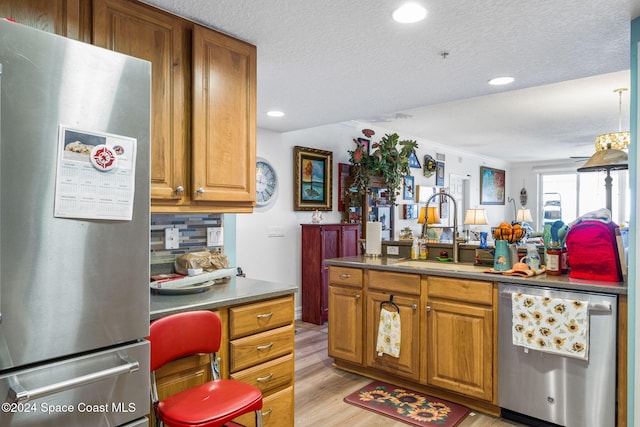 kitchen with sink, light wood-type flooring, a textured ceiling, tasteful backsplash, and stainless steel appliances