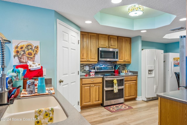 kitchen with decorative backsplash, a textured ceiling, stainless steel appliances, sink, and light hardwood / wood-style flooring