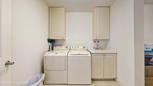 laundry area with cabinets, sink, washing machine and dryer, a textured ceiling, and light tile patterned flooring