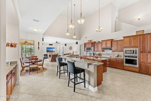 kitchen with ceiling fan with notable chandelier, pendant lighting, a kitchen bar, stainless steel appliances, and light stone countertops