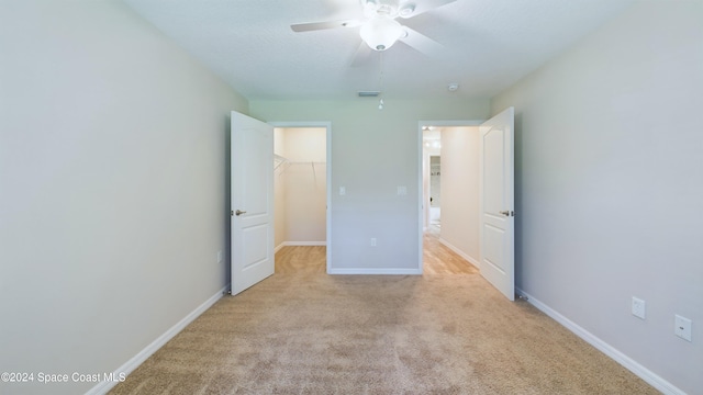 unfurnished bedroom featuring a walk in closet, ceiling fan, a closet, and light colored carpet