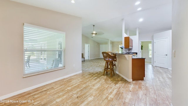 kitchen featuring sink, ceiling fan, light wood-type flooring, a kitchen bar, and kitchen peninsula