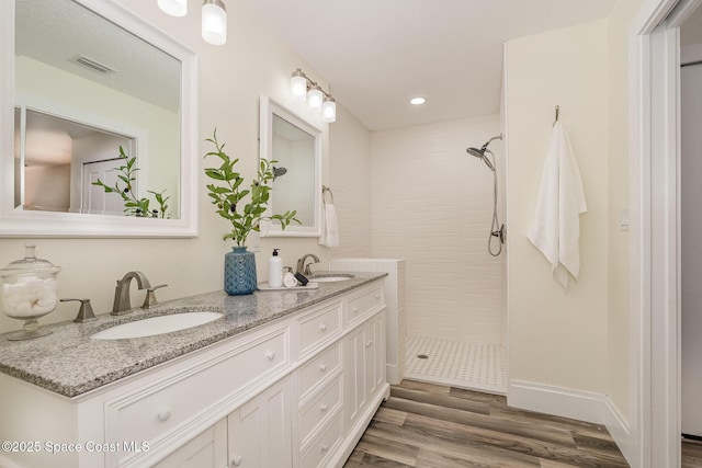 bathroom featuring wood-type flooring, vanity, and a tile shower