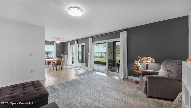 living room featuring ceiling fan, light tile patterned floors, a healthy amount of sunlight, and a textured ceiling