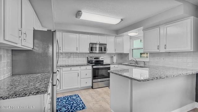 kitchen with kitchen peninsula, light stone countertops, white cabinets, and appliances with stainless steel finishes