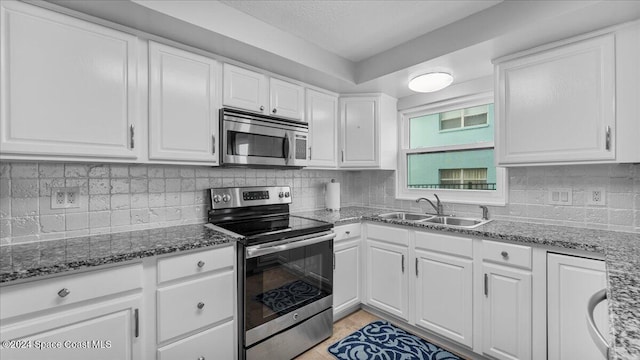 kitchen featuring decorative backsplash, stainless steel appliances, sink, dark stone countertops, and white cabinetry