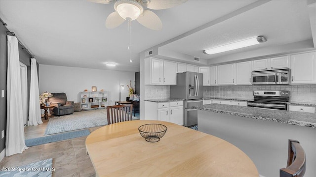 kitchen with white cabinets, backsplash, light stone countertops, and stainless steel appliances