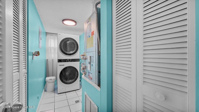 laundry room with light tile patterned floors, a textured ceiling, and stacked washer and clothes dryer