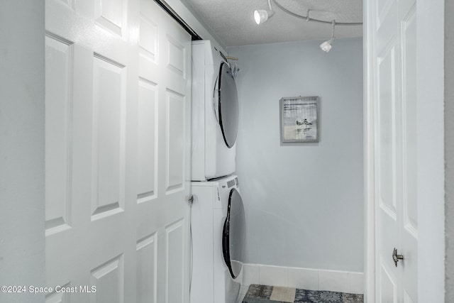 washroom featuring tile patterned flooring, stacked washer / drying machine, and a textured ceiling