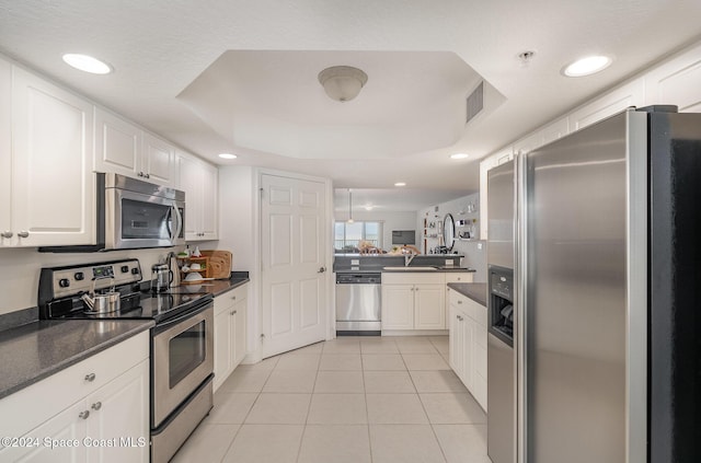 kitchen with appliances with stainless steel finishes, white cabinetry, a raised ceiling, and light tile patterned flooring