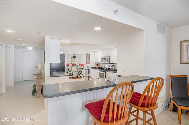 kitchen featuring stainless steel appliances, kitchen peninsula, a textured ceiling, a breakfast bar, and white cabinets