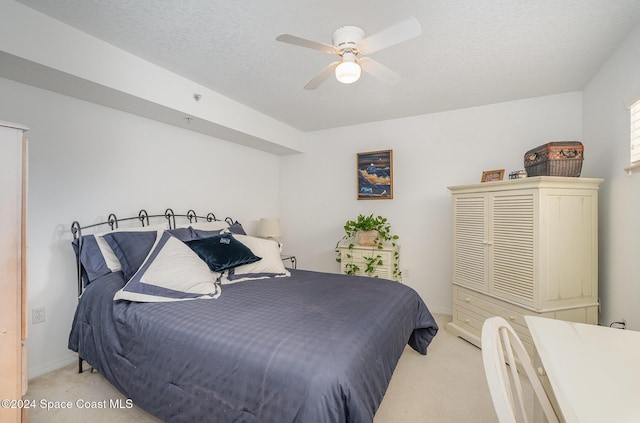 bedroom with ceiling fan, light colored carpet, and a textured ceiling