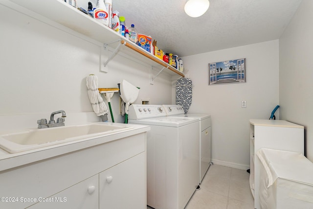 clothes washing area with cabinets, a textured ceiling, washer and clothes dryer, sink, and light tile patterned floors