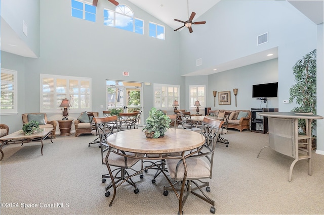 dining room with ceiling fan, a healthy amount of sunlight, light carpet, and high vaulted ceiling