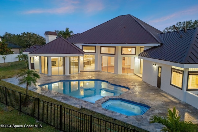 pool at dusk featuring a sunroom, a patio area, and an in ground hot tub