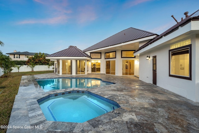 pool at dusk with a patio area and an in ground hot tub