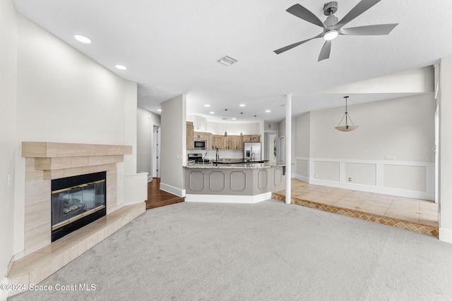 unfurnished living room featuring light carpet, ceiling fan, a fireplace, and sink