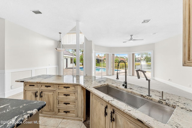 kitchen with a textured ceiling, ceiling fan, light stone counters, and sink