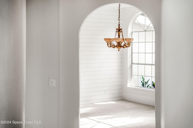 interior space with carpet flooring, wood walls, and an inviting chandelier