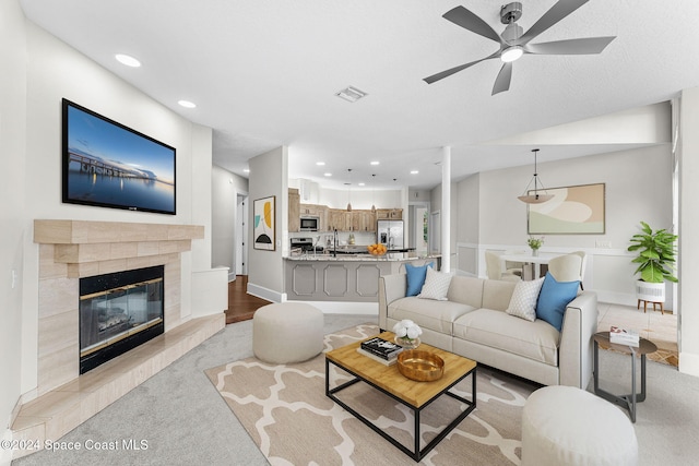 carpeted living room featuring a tile fireplace, ceiling fan, and sink